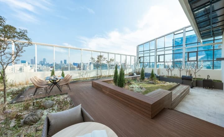 Expansive rooftop terrace with a wide wooden deck, planters, an outdoor dining set, a grill, and a panoramic city skyline view.