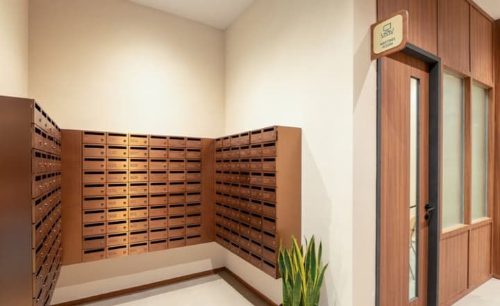 Residential lobby area with a large bank of secure, copper-toned mailboxes and a meeting room entrance with warm wood paneling.
