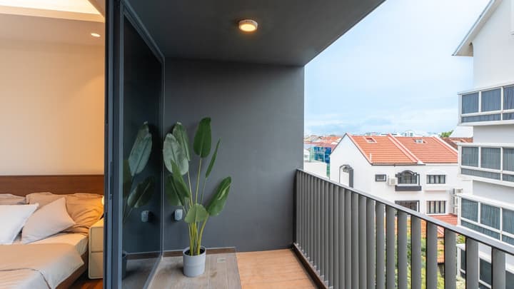Outdoor balcony with dark gray walls, a metal railing, a large potted plant, and a view of neighboring buildings with orange tile roofs.