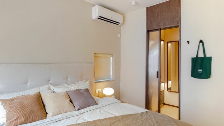 Neutral-toned bedroom with a queen bed and a unique small window niche, featuring a sliding glass door entrance to a compact walk-in closet area.