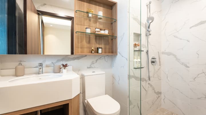 Modern bathroom featuring a glass-enclosed shower, a white vanity with an angular sink, and marble-patterned wall tiles.