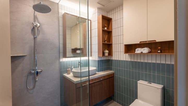 Modern full bathroom with a walk-in rain shower, wood vanity with an oval stone sink, and a two-toned wall with white and blue subway tiles.