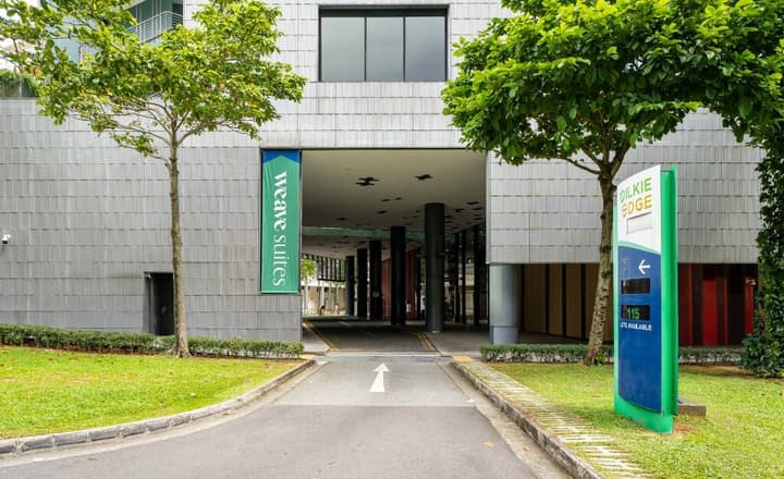 Exterior view of the building's driveway entrance with mature trees, a gray tiled facade, a Weave Suites banner, and a directional sign for Wilkie Edge.