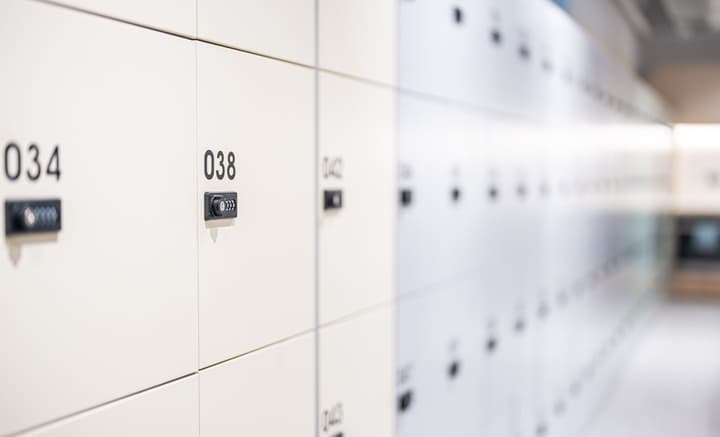 A long, receding perspective view of rows of bright, clean personal storage lockers. The lockers are numbered and secured with digital combination locks on the doors.