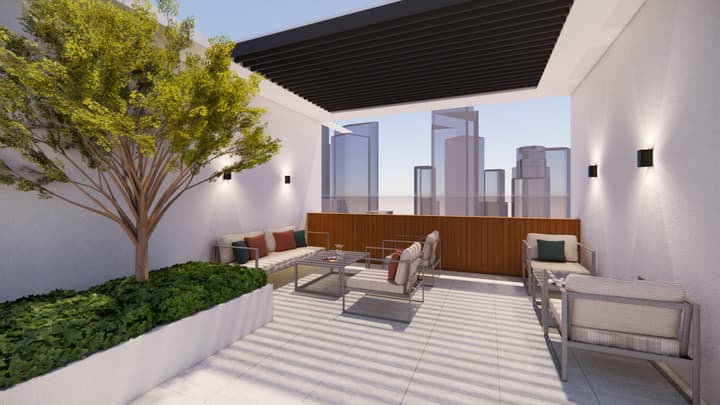 A sunny, private rooftop terrace with comfortable outdoor furniture, textured white walls, a large planted tree, and a panoramic view of the distant city skyline.