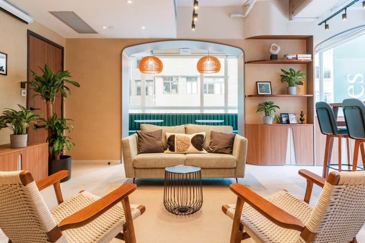 Modern, inviting lounge or common area featuring a neutral-colored sofa, two woven-rope accent chairs, a black wire side table, and an arched entryway leading to a turquoise upholstered window booth.