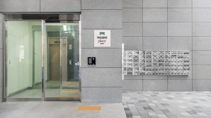 Building exterior featuring a glass entrance door, gray granite-style paneling, an intercom, and a large bank of small metal mailboxes mounted on the wall.