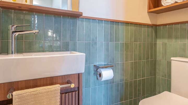 Small powder room detail with a white square sink, toilet, dark wood vanity, and vertical mint green tiled wall.