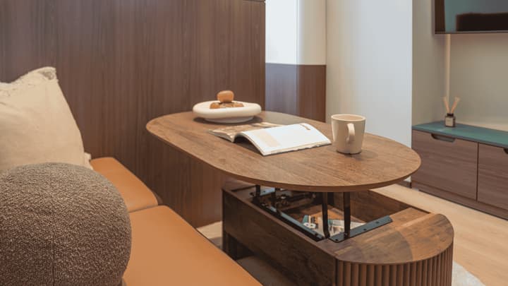 Close-up of a clever, lift-top wooden coffee table that transforms into a dining or workspace, set next to a brown leather sofa in the Premium Suite Queen living area.