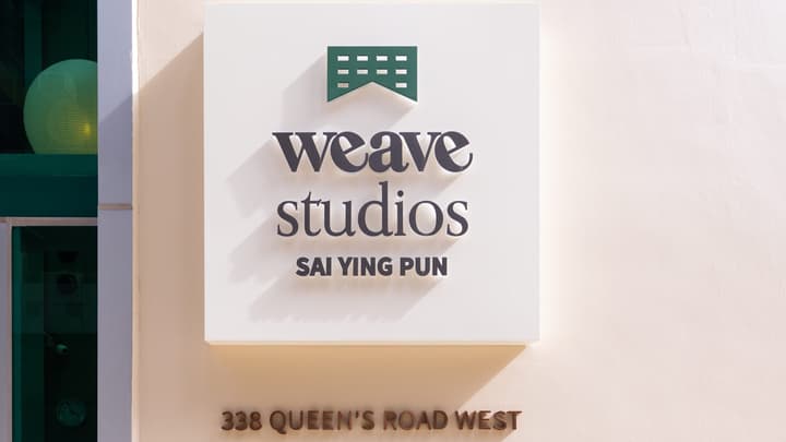 Close-up of the clean, white sign for 'Weave Studios Sai Ying Pun' with the property address '338 Queen's Road West' in bronze lettering.