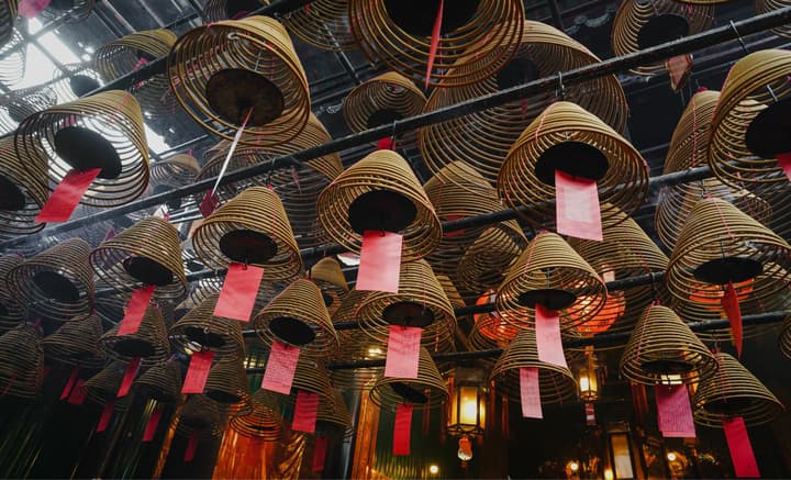 An upward-facing photo of large, spiraling incense coils with red tags hanging from the ceiling of a traditional Hong Kong temple.