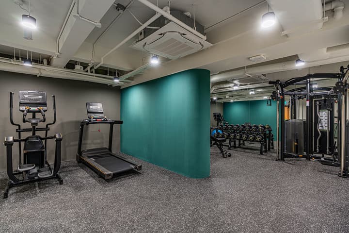 Well-equipped apartment gym with a treadmill, elliptical machine, rack of free weights, and a teal-colored curved accent wall.