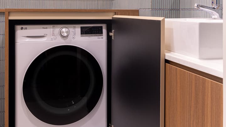 Close-up of a front-loading washer/dryer unit concealed behind a cabinet door in a modern bathroom area, next to a square sink.
