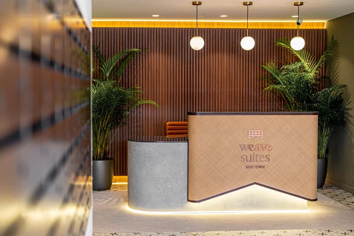 Modern reception desk with a rattan-paneled front, a concrete-textured base, warm wood slat wall paneling, and pendant lights.
