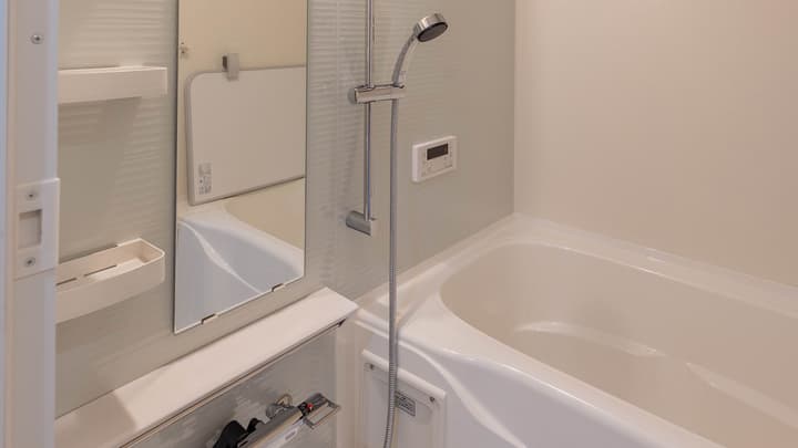 Bright, modern Japanese-style bathroom featuring a deep bathtub, a chrome shower on a rail, and a digital temperature control panel on the wall.