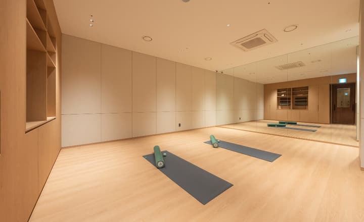 Clean, minimalist fitness studio with light wood floors, a full mirrored wall, and two yoga mats with foam rollers.