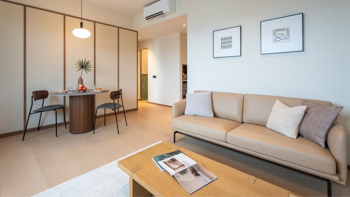 Living and dining area of a one-bedroom suite with a tan sofa, light wood floors, and a circular dining table set against a minimalist paneled wall.