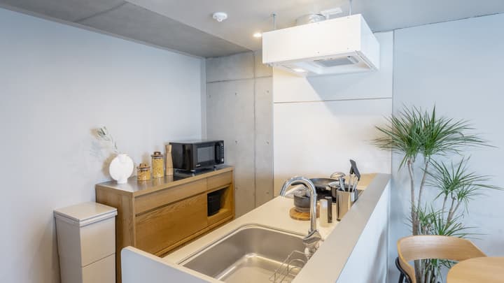 Detailed view of the kitchen counter with a sink, cooktop, small portable induction plate, and a wooden cabinet area with a microwave and exposed concrete above.