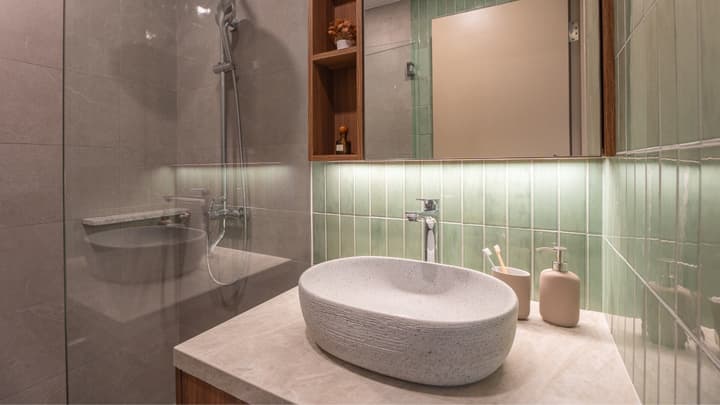 Close-up of a modern bathroom vanity with a textured oval basin sink, wood shelving, and vertical mint green tiled walls.