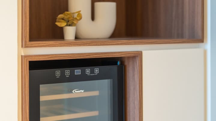 Close-up of a built-in wine cooler integrated into a wall unit with wood shelving and modern decorative accessories.