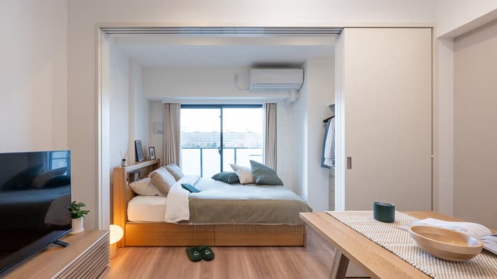 View of a bright bedroom separated from the main living area by sliding pocket doors, showing a wooden bed and balcony view.