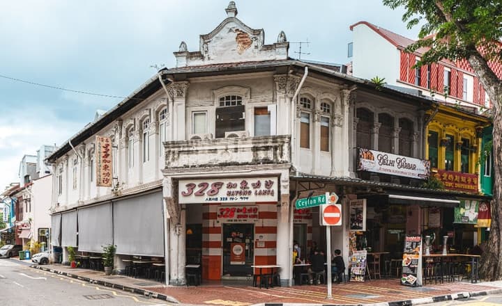 Corner street view of a traditional white two-story shophouse housing the famous 328 Katong Laksa restaurant on the ground floor.