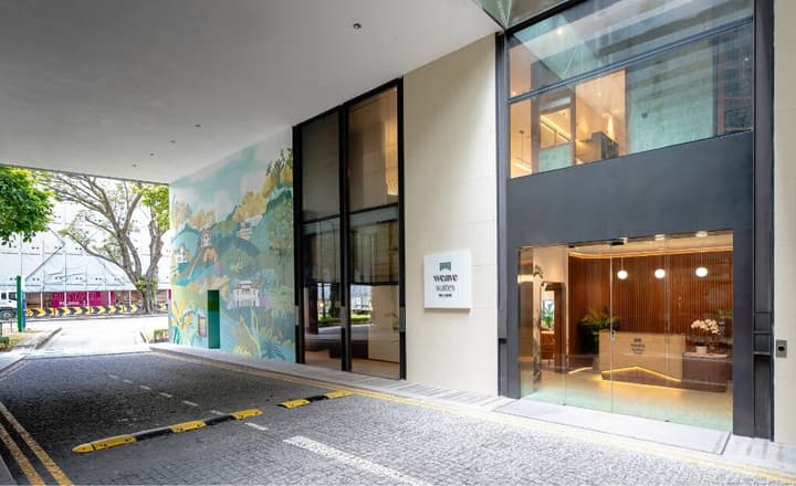 Exterior view of a co-living building entrance featuring a large, vibrant landscape mural, modern glass doors, and a sleek Weave Suites sign.