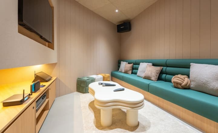 Dedicated karaoke and TV room with a curved, dark teal sofa, a unique white coffee table, and gaming consoles on a light wood cabinet.