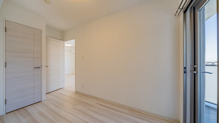 Empty bedroom featuring light wood-style flooring, white walls, light wood closet doors, a doorway into an inner room, and a sliding glass door leading to a balcony.