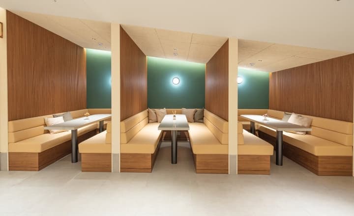 Three semi-private dining or meeting booths with high dividing walls, tan leather-look upholstery, and modern tables.