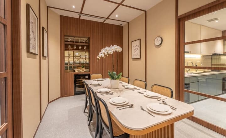 Private dining room featuring a long marble-topped table set for eight, rattan and wood chairs, warm wood wall paneling, and a built-in wine cooler and display.