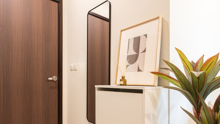 Residential entryway with a tall wooden door, white shoe cabinet, full-length black-framed mirror, and a piece of abstract framed artwork.
