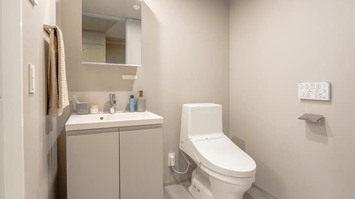 View of the separate toilet room featuring a small vanity sink with storage, a wall-mounted towel rack, and a modern Japanese washlet toilet.
