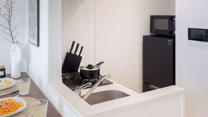 Close-up view of a compact kitchenette with a cooktop, sink, black fridge, microwave, and a knife block on the counter.