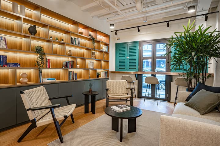 Cozy resident reading room with floor-to-ceiling wooden bookshelves, a soft rug, a light sofa, and bar-style seating by the window.
