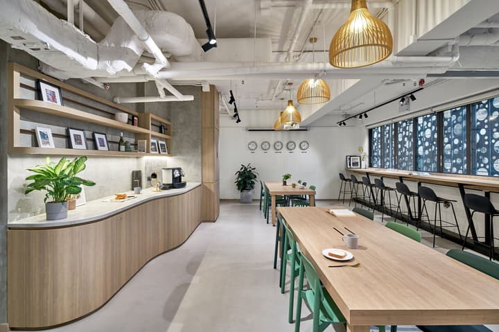 Long communal working and reading room with light wood tables, green chairs, bar-style window seating, and a modern coffee/snack bar area.