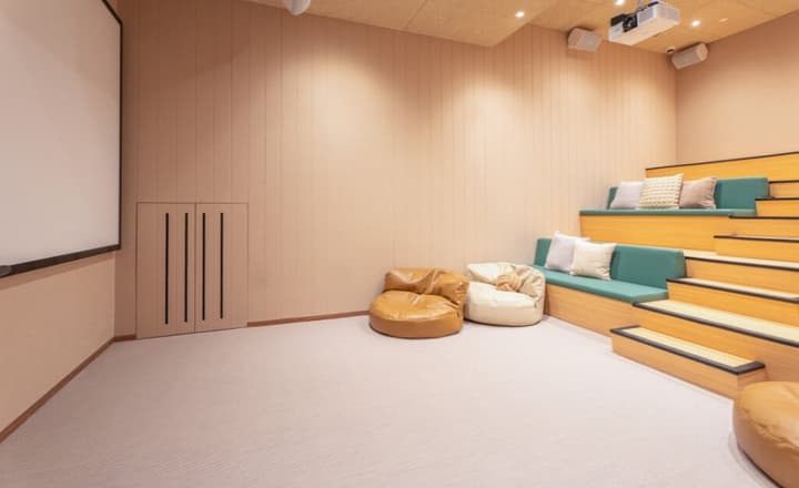 Residential movie theatre room with stepped seating featuring teal cushions, a projector screen, and comfortable brown and white beanbag chairs on a carpeted floor.