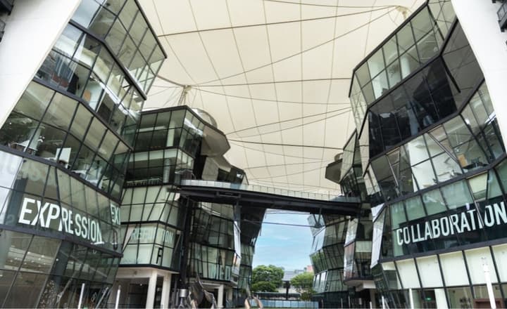 Modern, angular glass architecture of the LASALLE College of the Arts campus, with large words like "EXPRESSION" and "COLLABORATION" on the facade.
