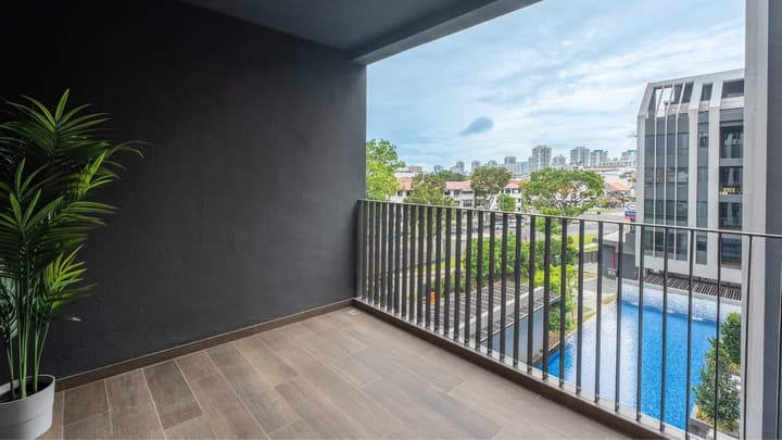 Outdoor balcony with dark grey walls, wood-look tiled floor, and metal railing overlooking a swimming pool and a distant city skyline.