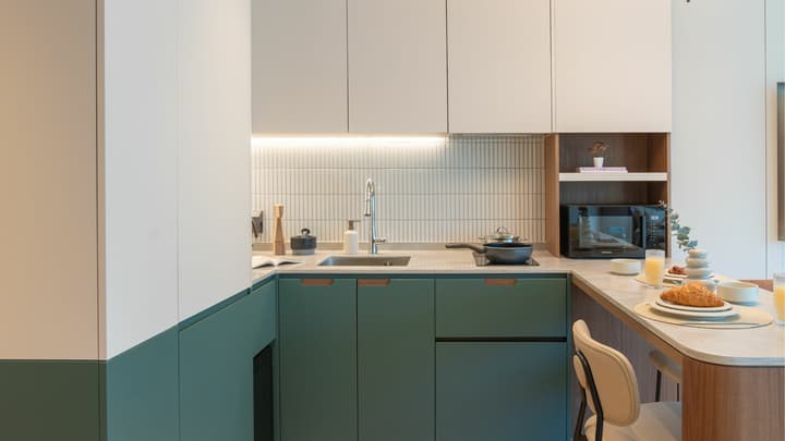 Close-up of the fully equipped L-shaped kitchenette in the Junior Luxe Suite, featuring forest green lower cabinets, a microwave in a wood-toned cubby, and white vertical subway tile backsplash.