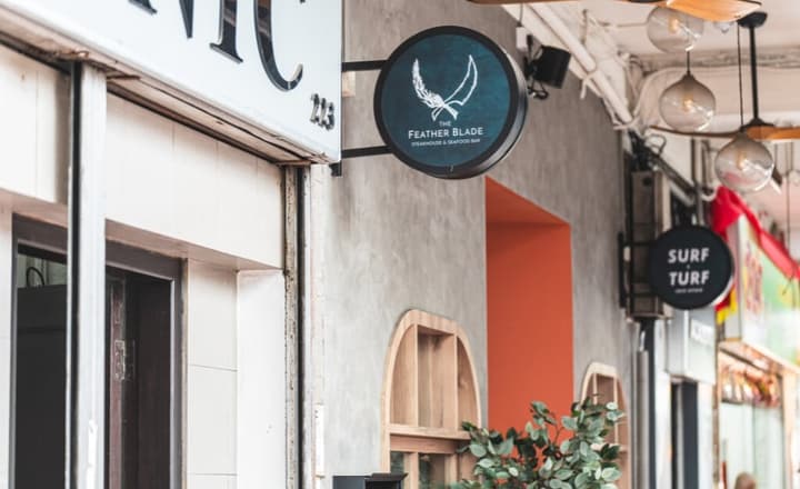 Close-up of a commercial street with hanging circular signs for two dining establishments, The Feather Blade steakhouse and Surf Turf bar.