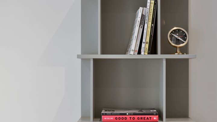 Close-up of a modern, gray built-in bookshelf displaying books, including 'Good to Great,' and a vintage-style gold and black round clock.