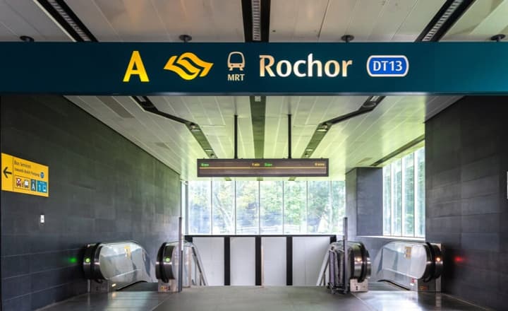 Rochor MRT station entrance with the DT13 station signage visible above the escalators leading down, featuring dark walls and bright lighting.