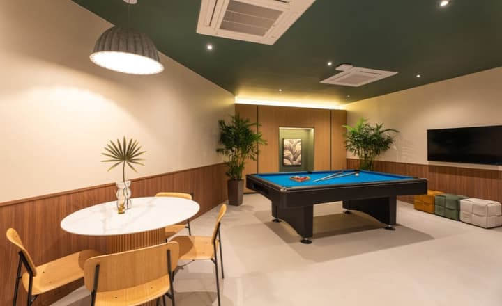 Spacious entertainment room featuring a pool table, dark green accent ceiling, wood wainscoting, and a small white marble table with lounge chairs.