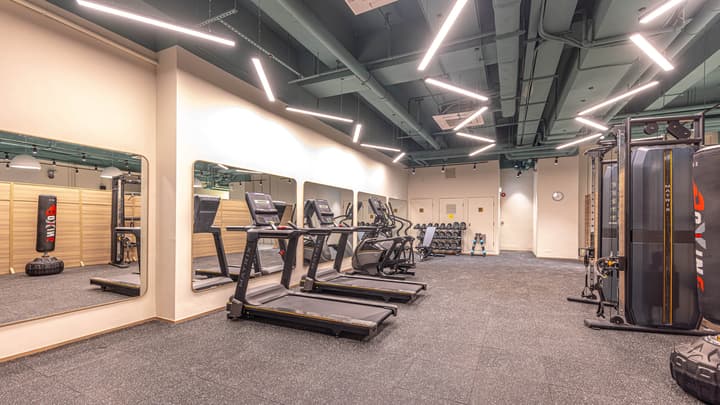 Indoor fitness center with black rubber flooring, two treadmills, an elliptical machine, mirrored walls, a weights rack, and a punching bag.