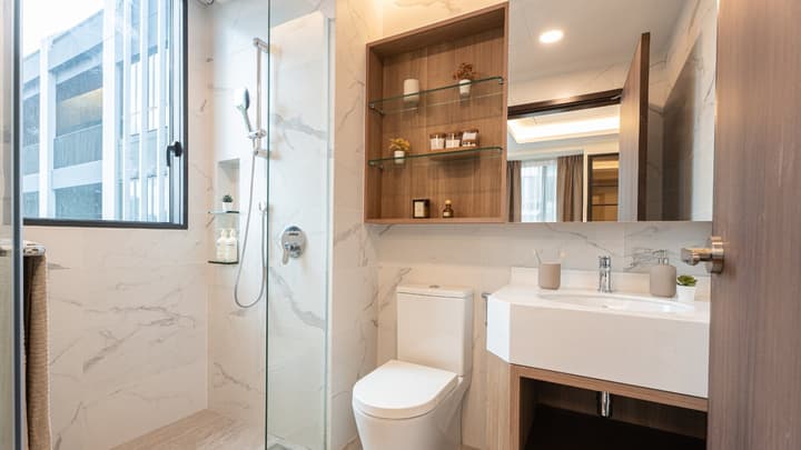 Modern bathroom with a glass-enclosed shower, white marble-style wall tiles, white vanity with a rectangular sink, and built-in shelving.