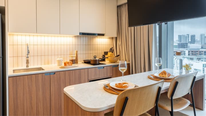 Kitchen and dining bar area with a meal set up for two, highlighting the wood cabinetry, beige tile backsplash, and the expansive city view through the full-height window.