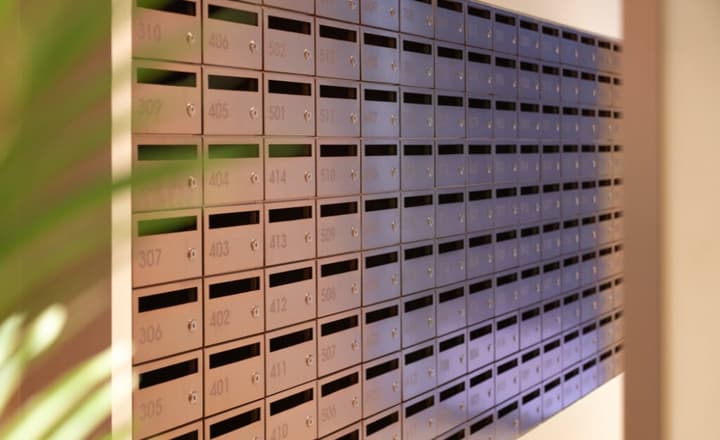A wall of curved, metallic mailboxes with individual locks and engraved numbers, angled toward a soft light source.