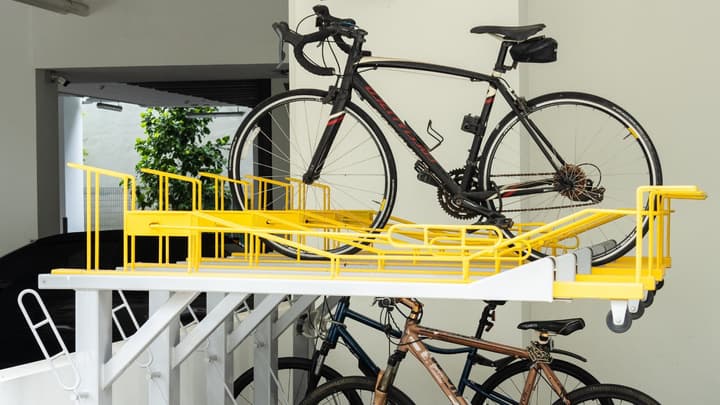 A close-up of a two-tier, yellow and white vertical bicycle parking rack with a black road bike secured on the top level.