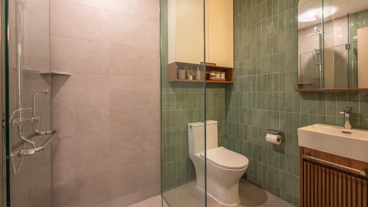 Modern bathroom with a glass-enclosed walk-in shower, toilet, vanity with wood paneling, and a sage green vertical subway tile accent wall.